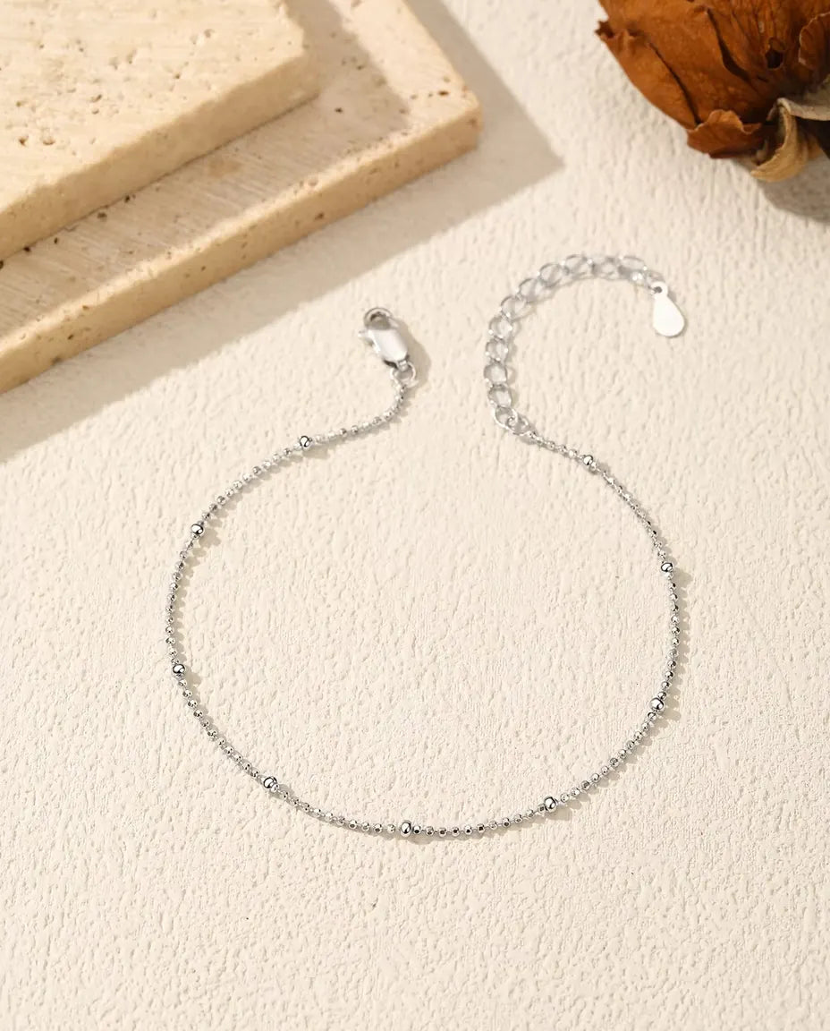 Bracciale Catena a Palline in Argento 925 - disteso su una superficie chiara ruvida, con chiusura e prolunga