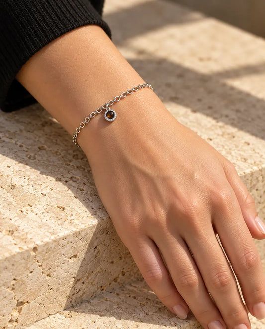 Donna che indossa al polso il bracciale argentato con charm tondo e zirconi, alla luce calda del sole