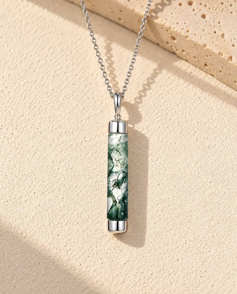 Collana Agata Muschiata Cilindro Lungo in Argento 925 - appoggiata su una superficie chiara ruvida accanto a un blocco di travertino