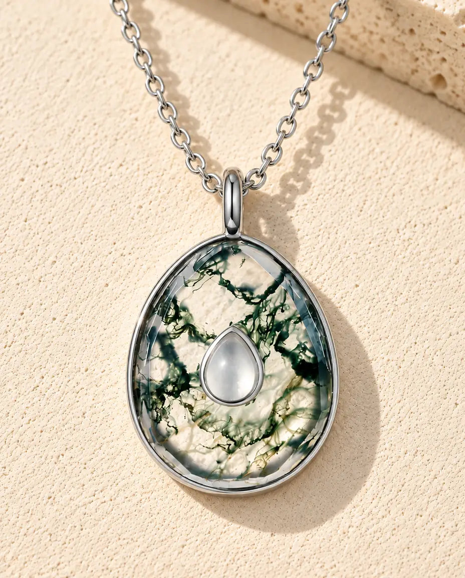 Collana con Ciondolo a Uovo in Agata Muschiata e Argento 925 - appoggiata su una superficie chiara ruvida accanto a un blocco di travertino
