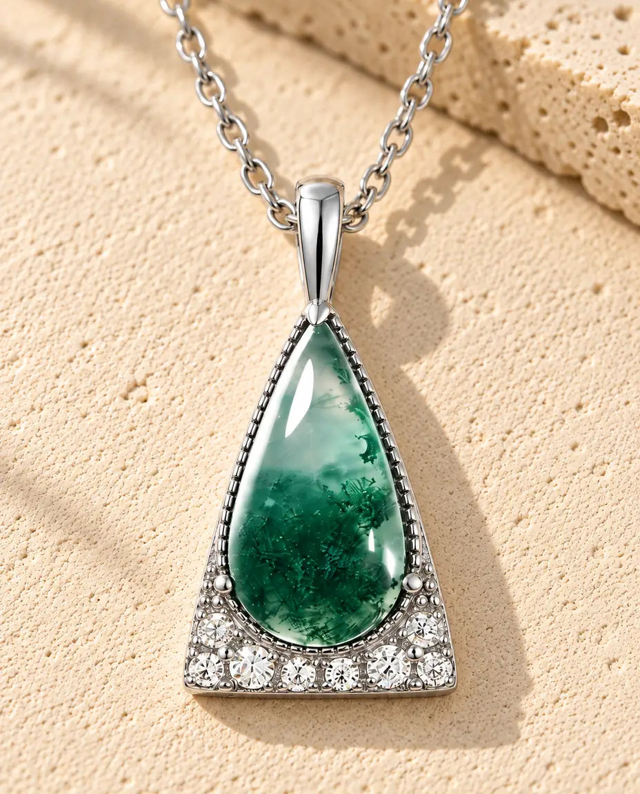 Collana Agata Muschiata Triangolo in Argento 925 - appoggiata su una superficie chiara ruvida accanto a un blocco di travertino