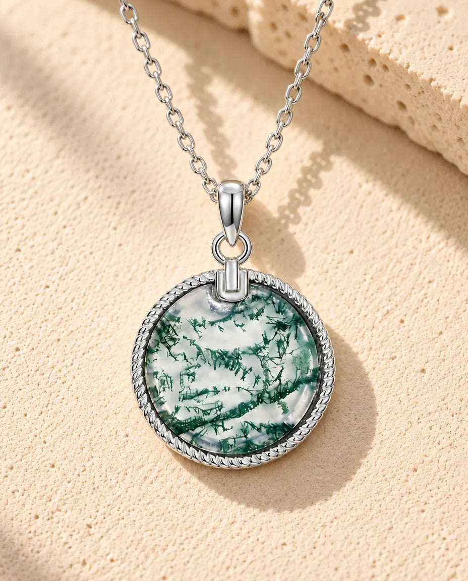 Collana Agata Muschiata Medaglione Rotondo in Argento 925 - appoggiata su una superficie chiara ruvida accanto a un blocco di travertino
