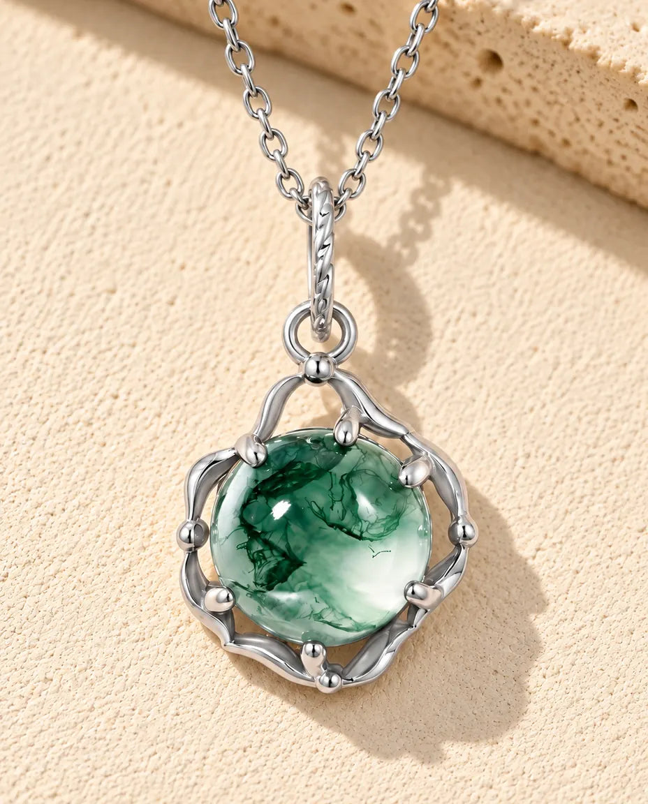 Collana Agata Muschiata Tonda in Argento 925 - appoggiata su una superficie chiara ruvida accanto a un blocco di travertino
