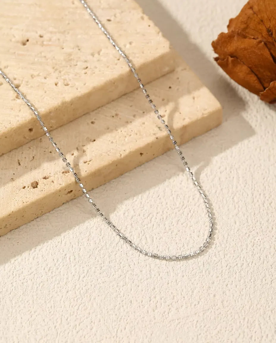 Collana Catena Diamantata in Argento 925 - adagiata su una superficie chiara accanto a una lastra di travertino