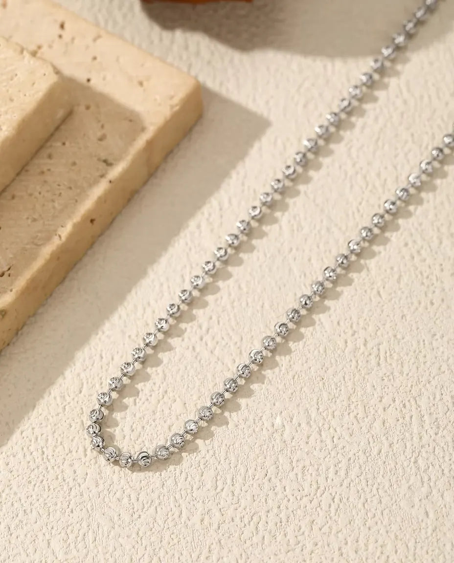 Collana di Palline Sfaccettate in Argento 925 - adagiata su una superficie chiara accanto a una lastra di travertino