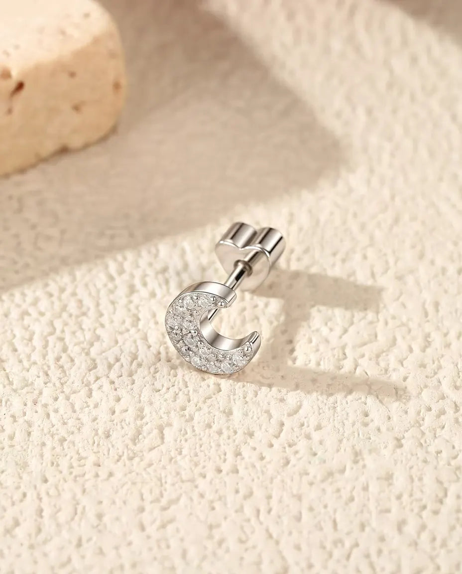 Orecchini a Mezzaluna con Pavé di Moissanite in Argento 925 - appoggiato di lato su una superficie chiara ruvida, chiusura a forma di cuore sul perno