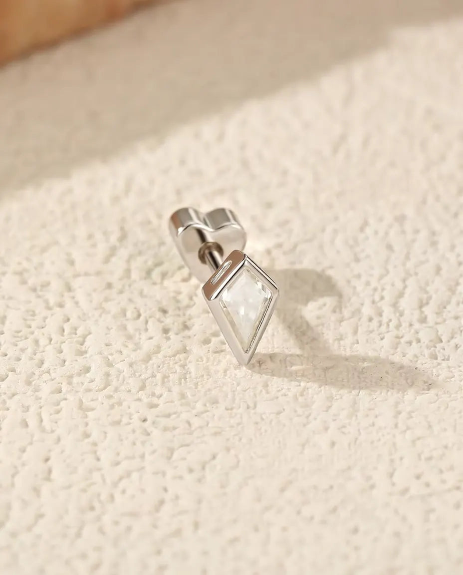 Orecchini con Moissanite Taglio Aquilone in Argento 925 - appoggiato di lato su una superficie chiara ruvida, chiusura a forma di cuore sul perno