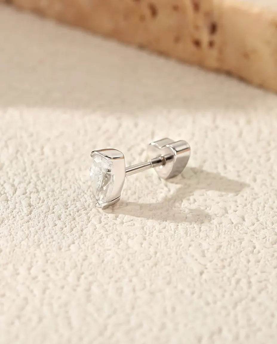 Orecchini con Moissanite a Goccia in Argento 925 - su una superficie chiara ruvida accanto a una lastra di travertino