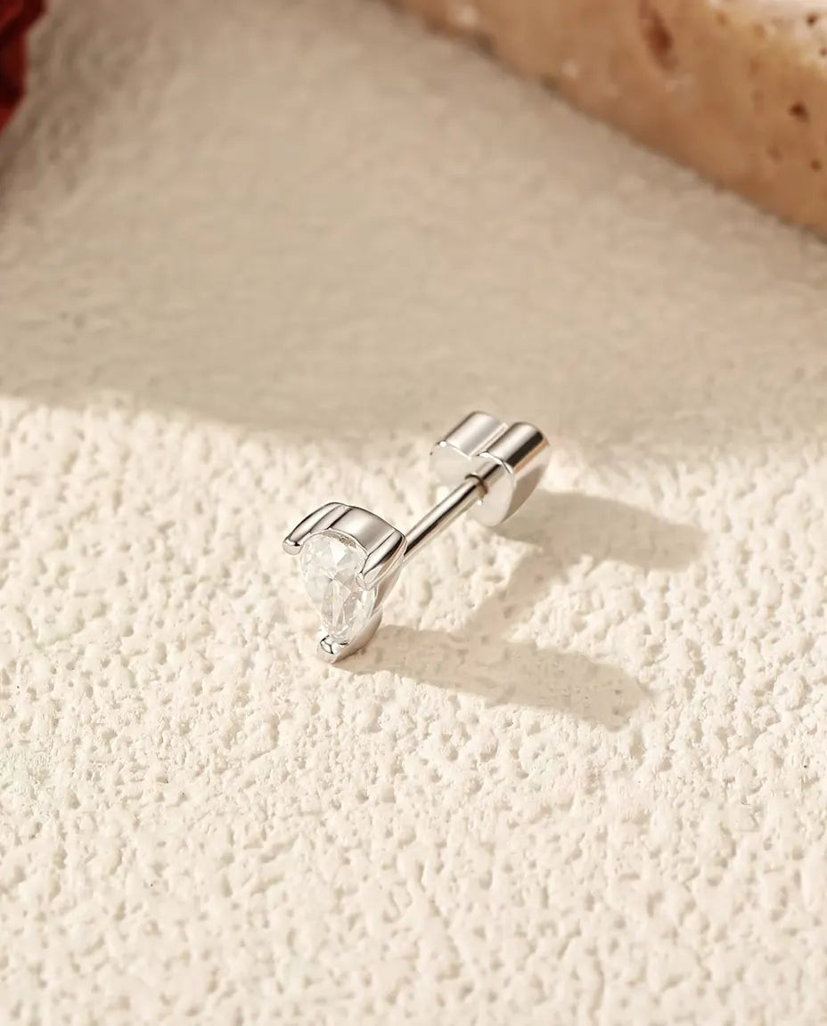 Orecchini con Moissanite a Goccia e Due Griffe in Argento 925 - appoggiato di lato su una superficie chiara ruvida, chiusura a forma di cuore sul perno