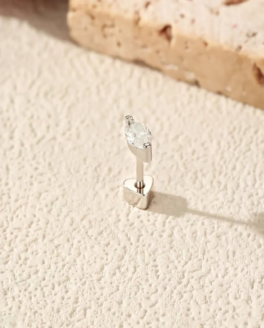 Orecchini con Moissanite Marquise a Mezzo Castone in Argento 925 - in piedi sulla chiusura a forma di cuore, su una superficie chiara ruvida