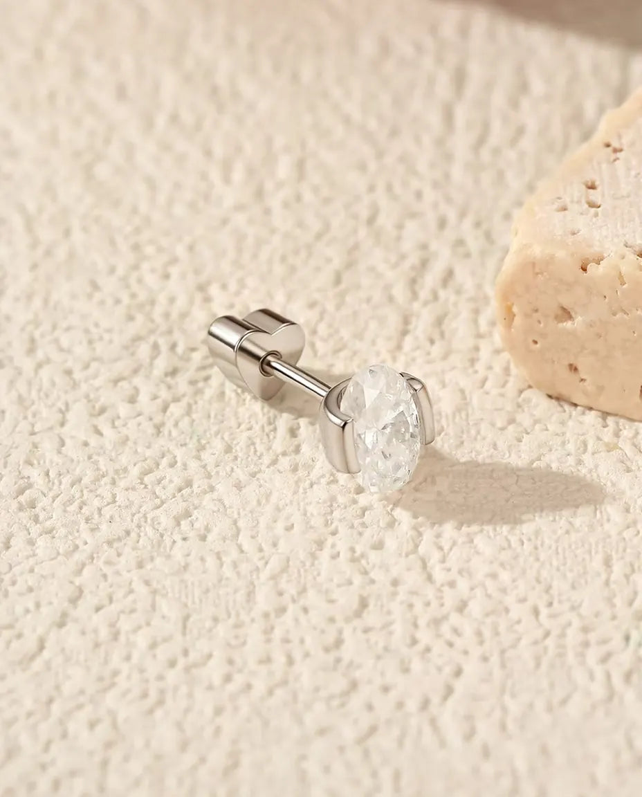 Orecchini con Moissanite Ovale a Incastonatura Laterale in Argento 925 - appoggiato di lato su una superficie chiara ruvida, chiusura a forma di cuore sul perno