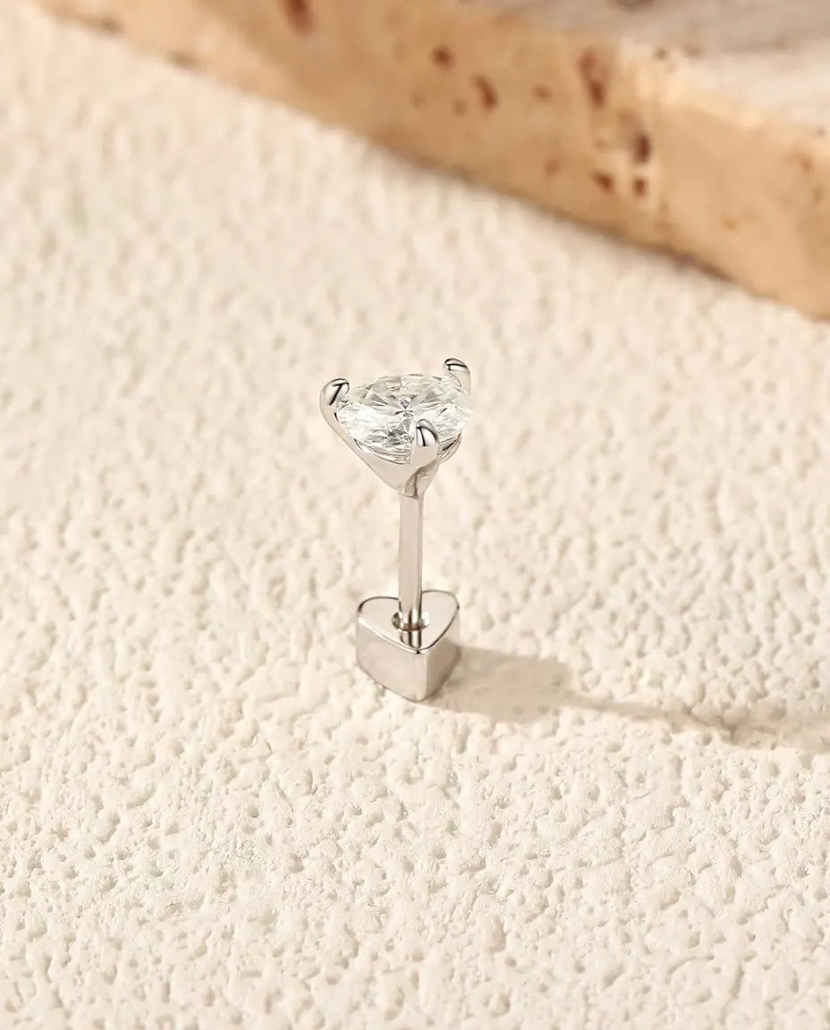 Orecchini Punto Luce con Moissanite Tonda a Tre Griffe in Argento 925 - in piedi sulla chiusura a forma di cuore, su una superficie chiara ruvida