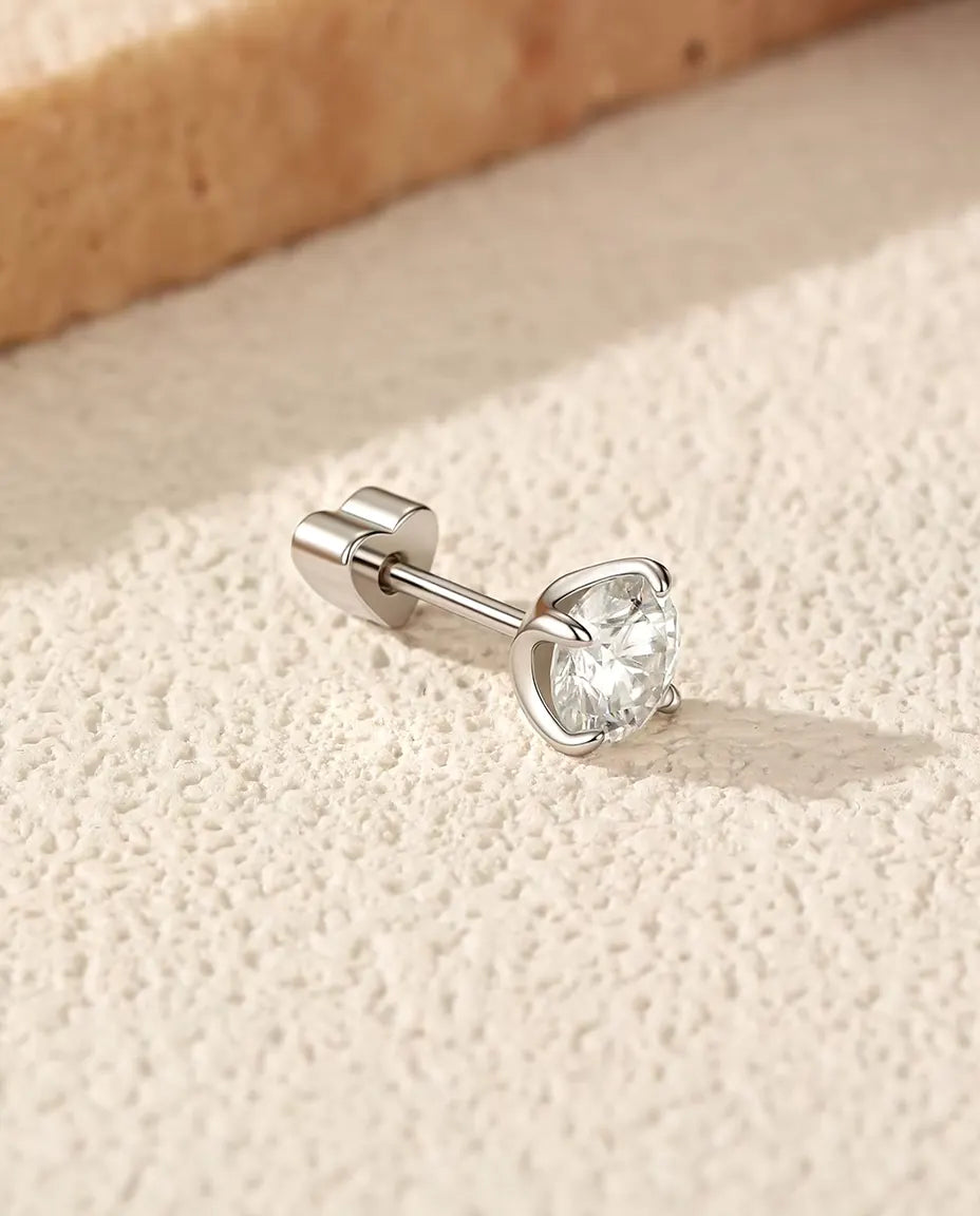 Orecchini Solitario con Moissanite da 5 mm a Quattro Griffe in Argento 925 - appoggiato di lato su una superficie chiara ruvida, chiusura a forma di cuore sul perno