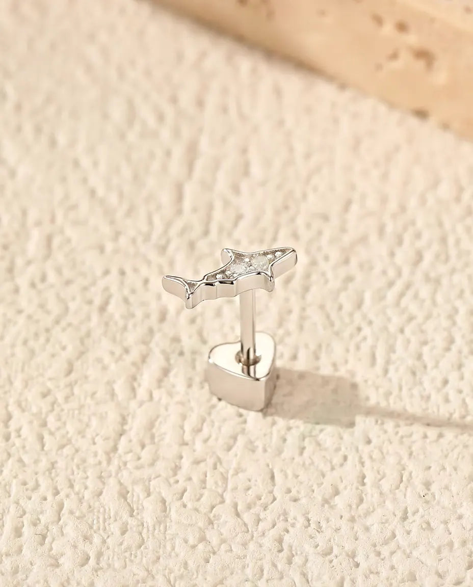 Orecchini a Forma di Squalo con Moissanite in Argento 925 - in piedi sulla chiusura a forma di cuore, su una superficie chiara ruvida