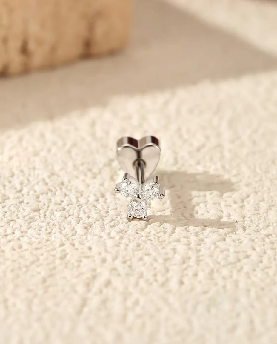 Orecchini a Trifoglio con Moissanite in Argento 925 - in piedi sulla chiusura a forma di cuore, su una superficie chiara ruvida