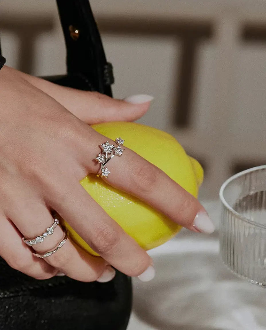 Anello Moissanite Stelle in Argento 925 - indossato insieme ad altri anelli, mano che tiene un limone