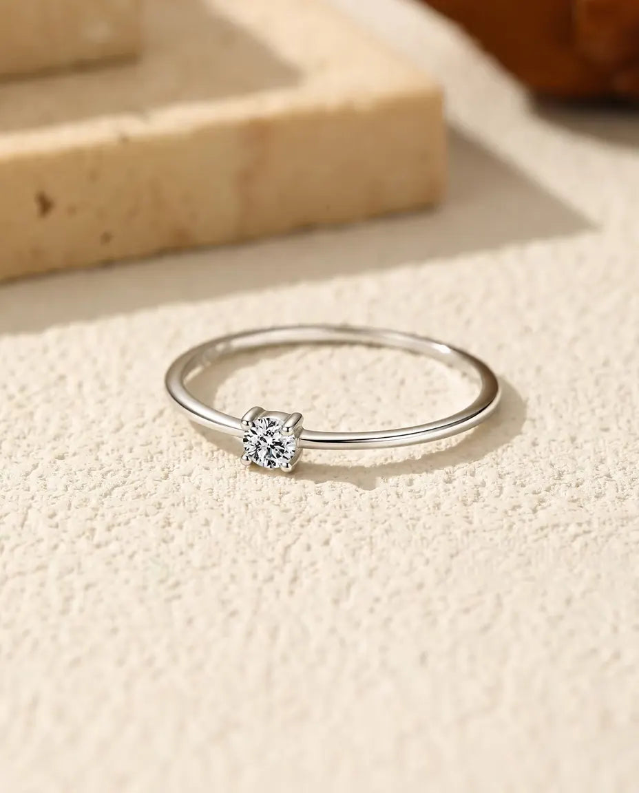 Anello Solitario Moissanite Sottile in Argento 925 - appoggiato in piano su una superficie chiara ruvida
