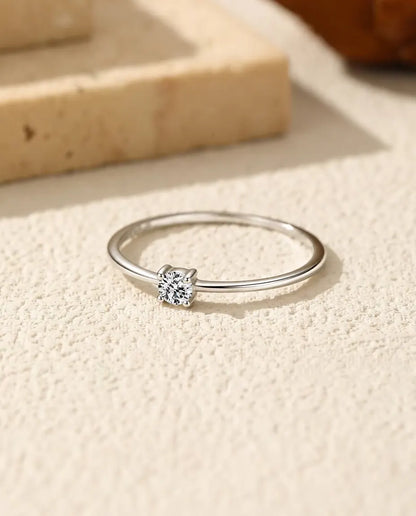 Anello Solitario Moissanite Sottile in Argento 925 - appoggiato in piano su una superficie chiara ruvida