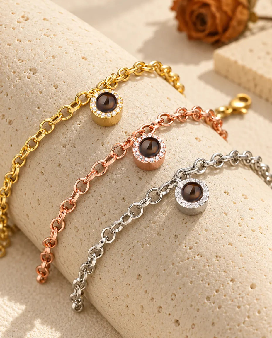 Tre bracciali con charm tondo a pavé nei colori dorato, color oro rosa e argentato, sul travertino