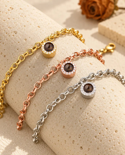 Tre bracciali con charm tondo a pavé nei colori dorato, color oro rosa e argentato, sul travertino