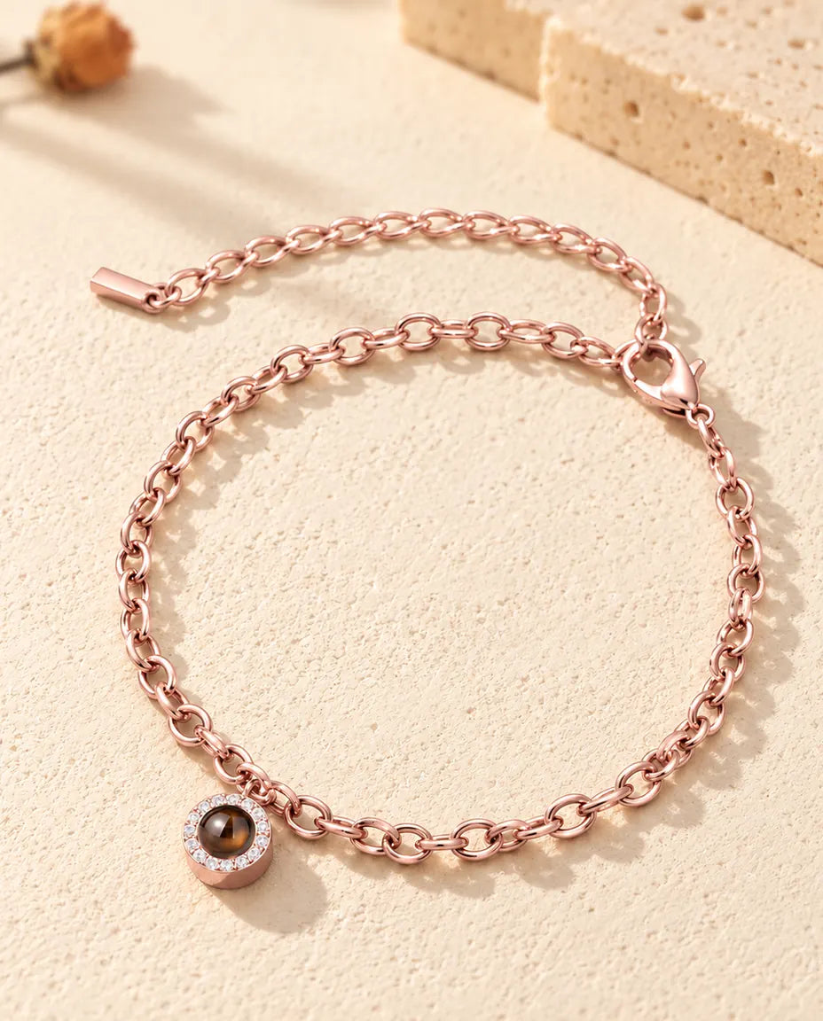 Bracciale color oro rosa con charm tondo a pavé, chiusura a moschettone e catenina di prolunga