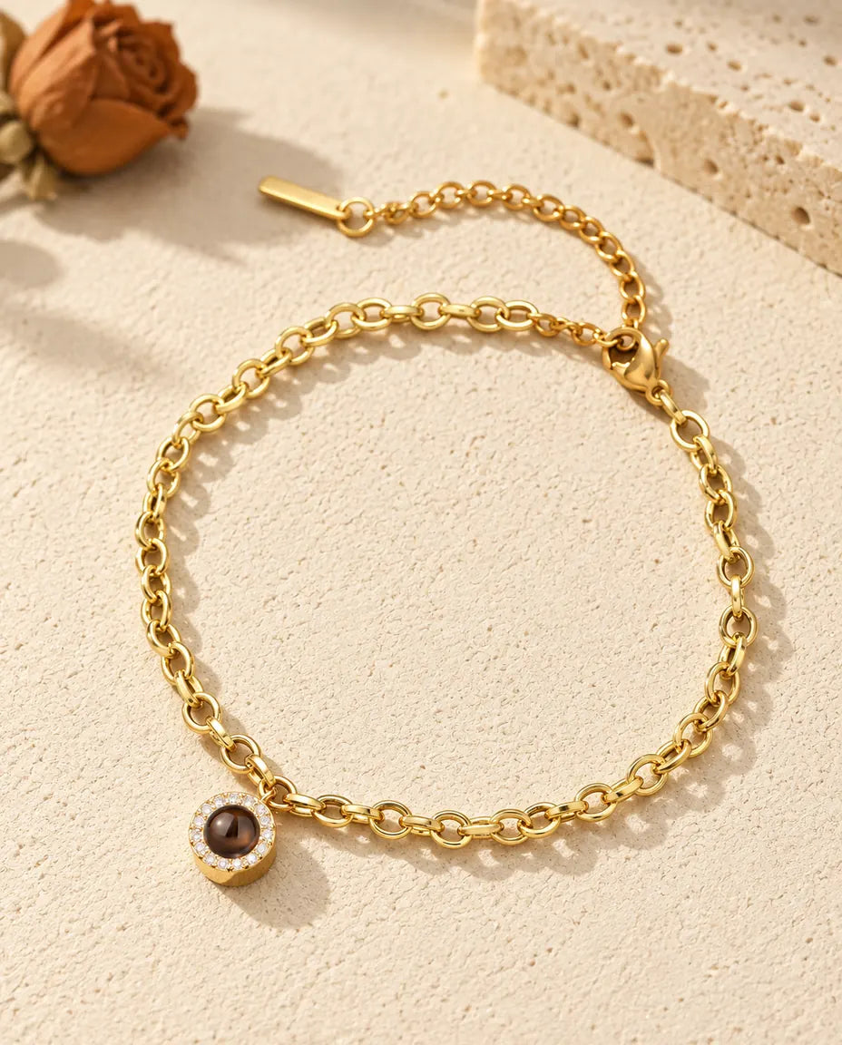 Bracciale con foto dentro dorato con charm tondo a pavé di zirconi, posato sul gesso color crema