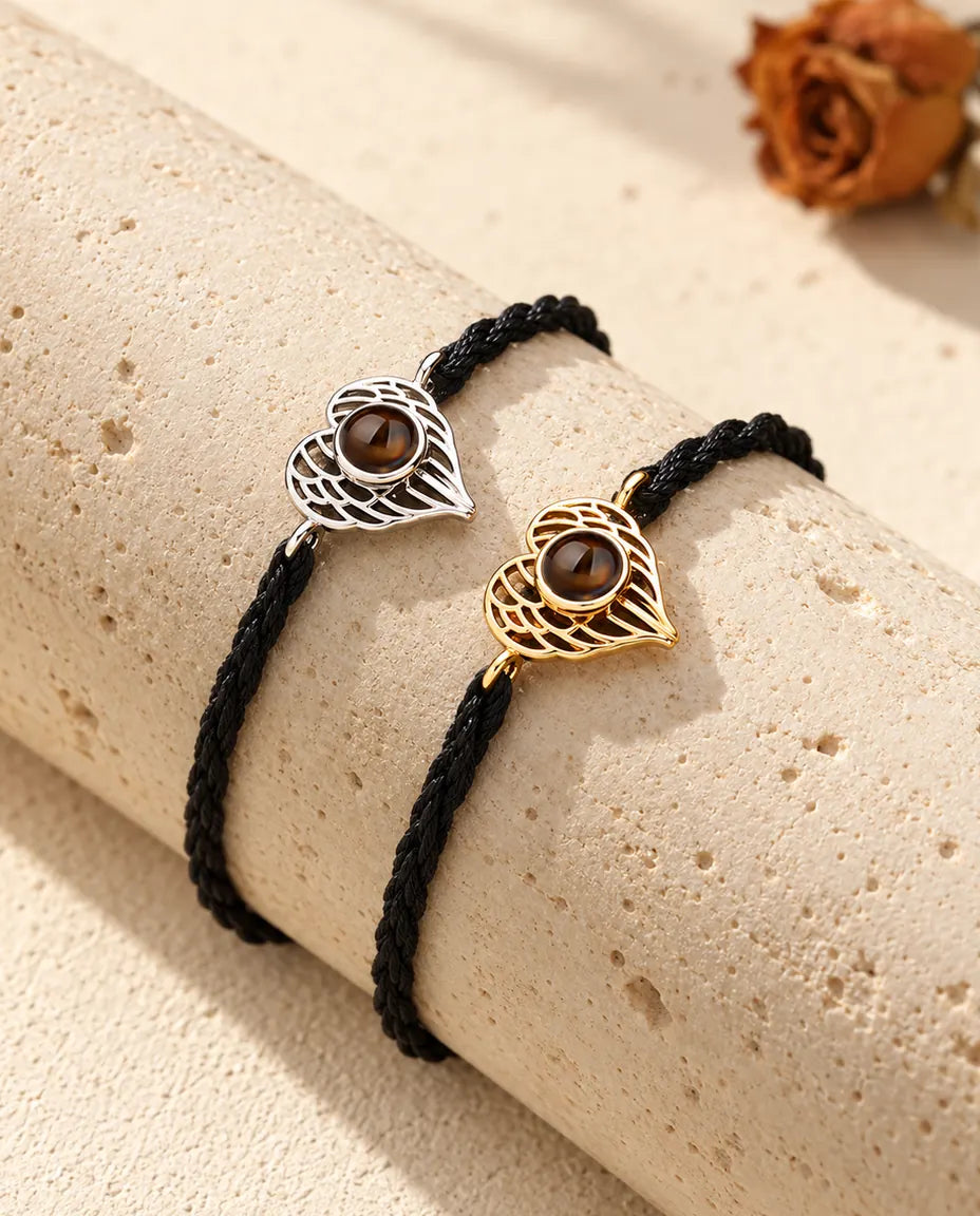Bracciali con cuore ad ali d'angelo argentato e dorato, uno accanto all'altro su un blocco di travertino