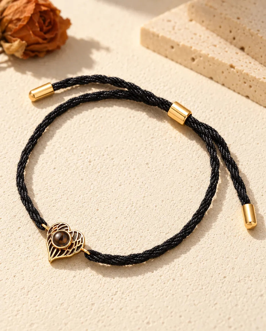 Bracciale ricordo dorato con cuore ad ali d'angelo su cordino nero ritorto, con passante e terminali
