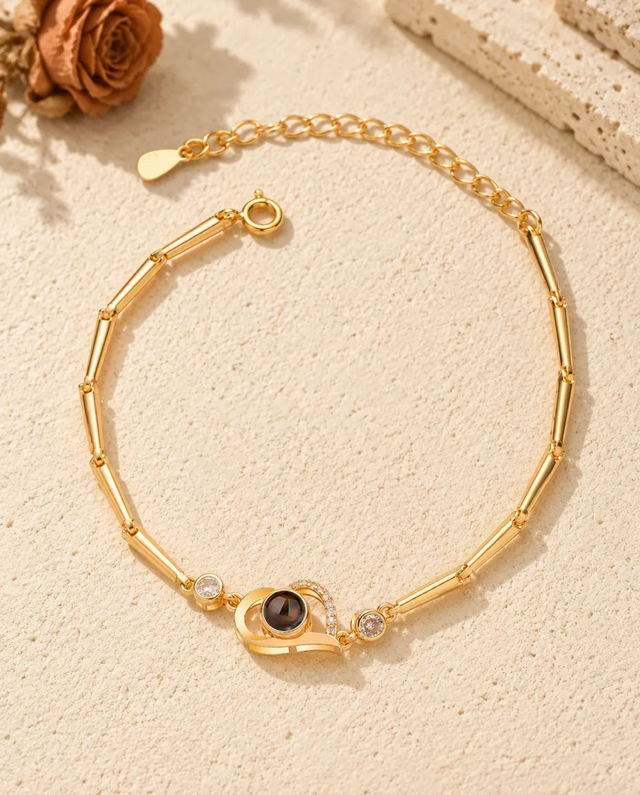 Vista dall'alto del bracciale dorato con cuore aperto e foto dentro, sul gesso crema