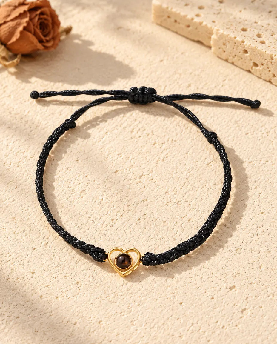 Vista dall'alto del bracciale con cuore aperto dorato su cordino intrecciato nero e nodo scorrevole