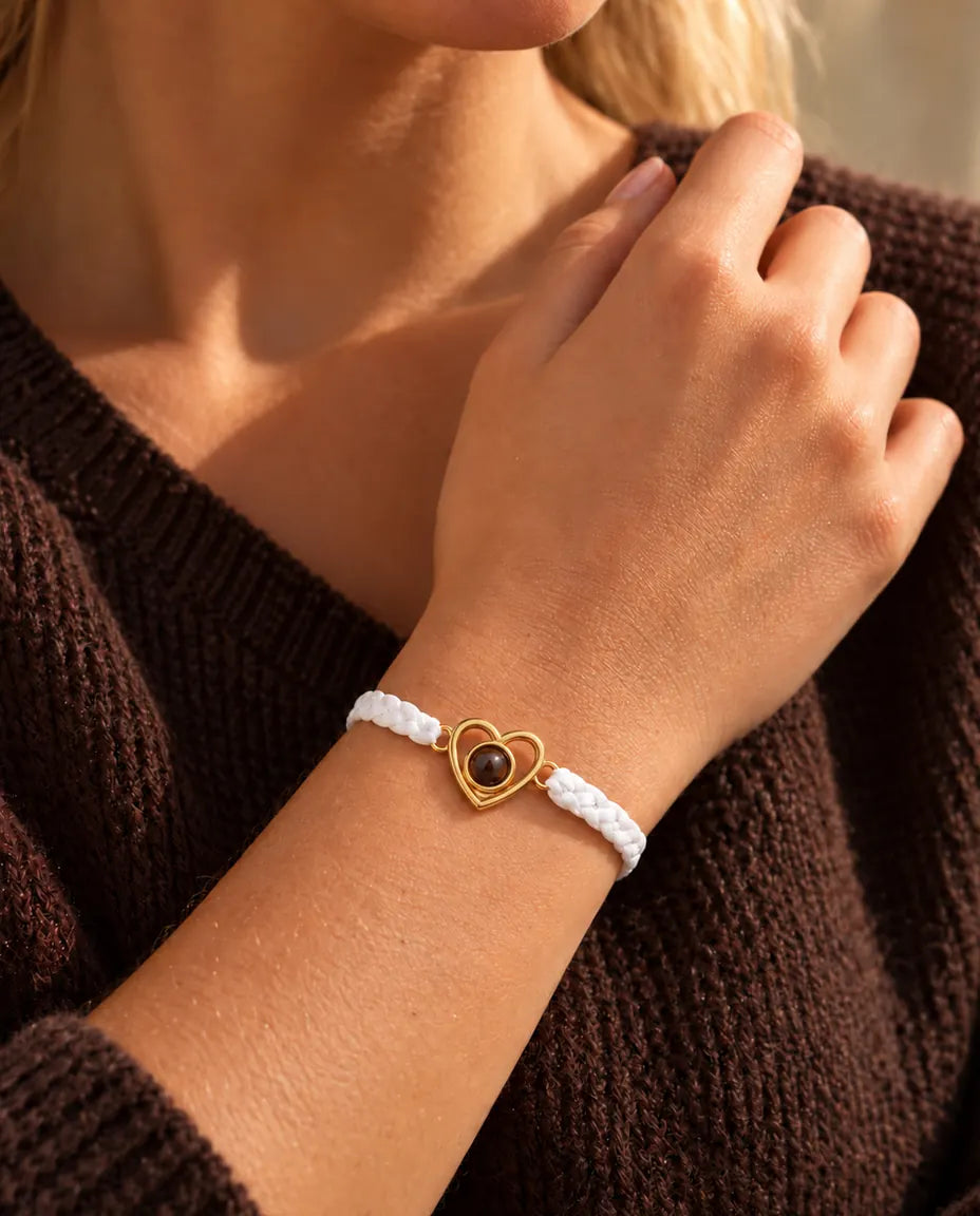 Primo piano del charm a cuore aperto dorato su cordino intrecciato bianco, con le dita sullo scollo