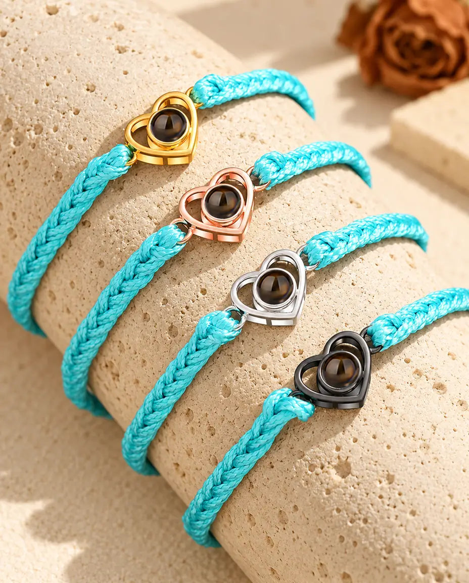 Quattro bracciali su cordino blu con cuore aperto dorato, color oro rosa, argento e nero su travertino