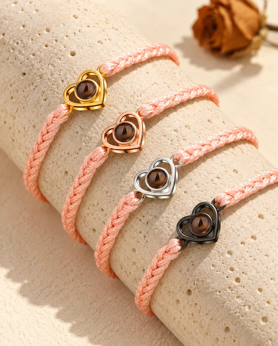 Bracciali su cordino intrecciato rosa con cuore aperto in tutti i colori, adagiati sul travertino