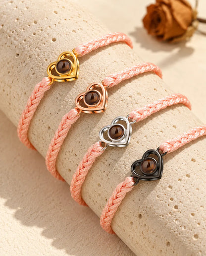 Bracciali su cordino intrecciato rosa con cuore aperto in tutti i colori, adagiati sul travertino