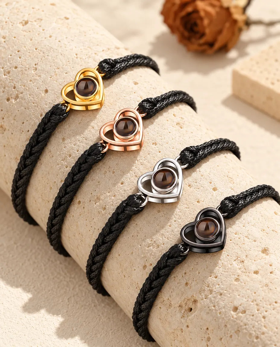 Quattro bracciali su cordino intrecciato nero con cuore aperto in ogni colore su un blocco di travertino