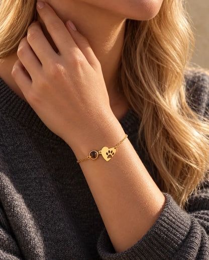 Primo piano del bracciale dorato con cuore e impronta di zampa al polso, dita sul lato del collo