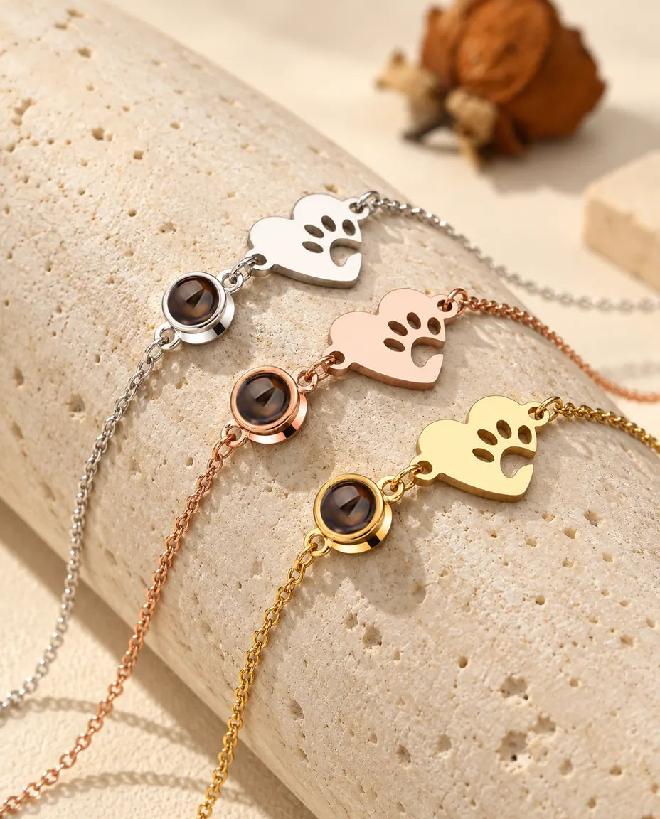 Tre bracciali con cuore e impronta di zampa, argentato, color oro rosa e dorato, su un blocco di travertino