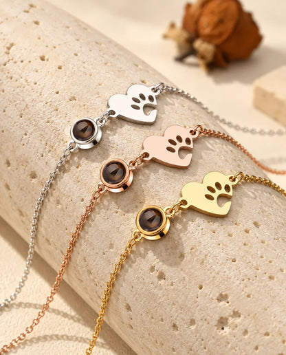 Tre bracciali con cuore e impronta di zampa, argentato, color oro rosa e dorato, su un blocco di travertino