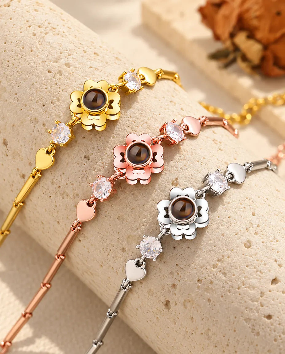 Tre bracciali con fiore quadrifoglio, dorato, color oro rosa e argentato, su un blocco di travertino