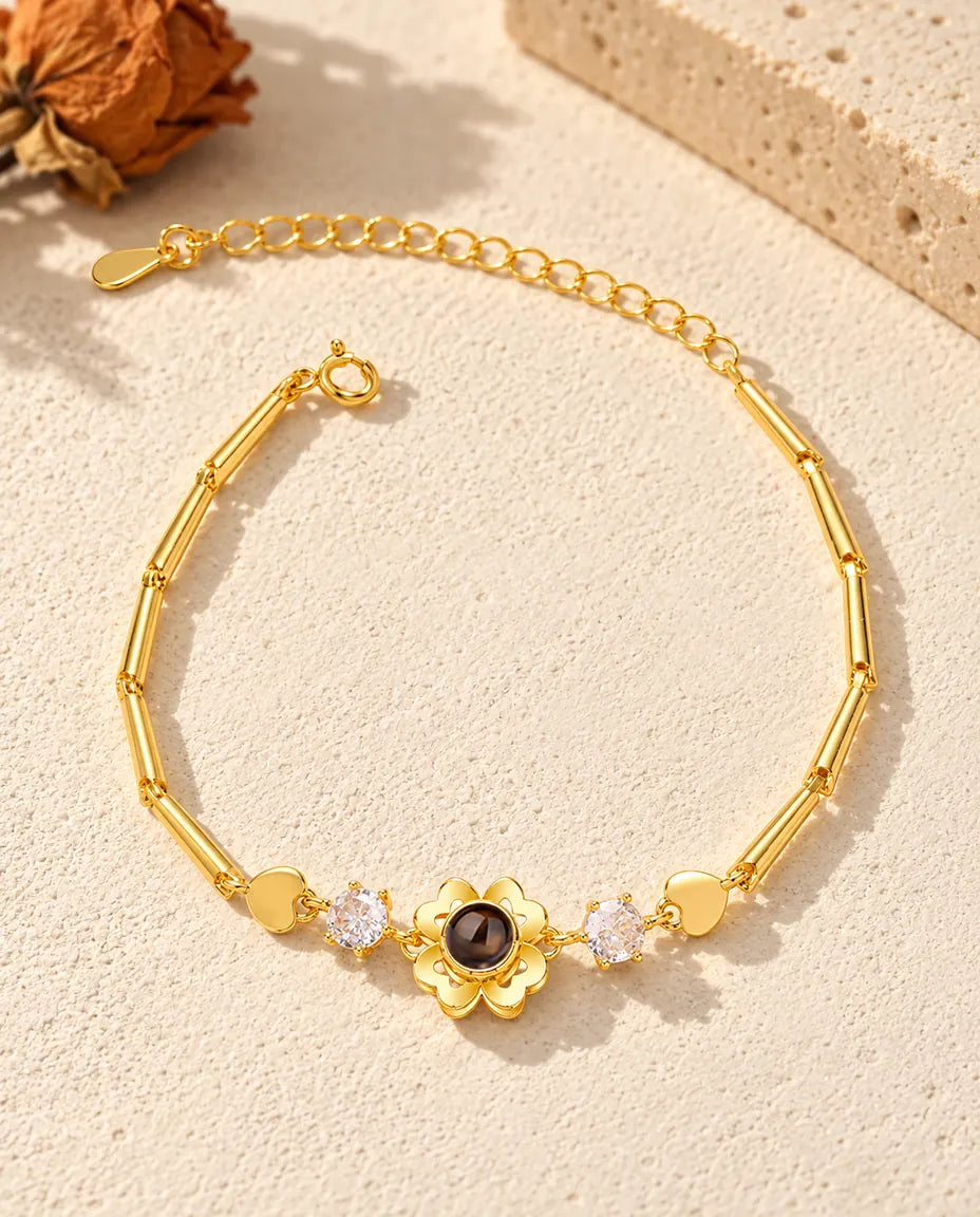 Vista dall'alto del bracciale dorato con fiore quadrifoglio e foto dentro, sul gesso crema