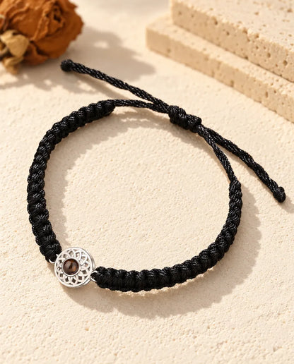 Bracciale con foto dentro: charm tondo traforato argentato su cordino intrecciato nero, sul gesso crema