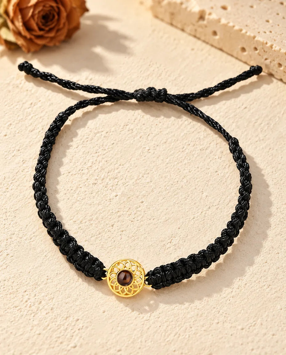 Vista dall'alto del bracciale con charm tondo dorato su cordino intrecciato nero, con nodo scorrevole e code