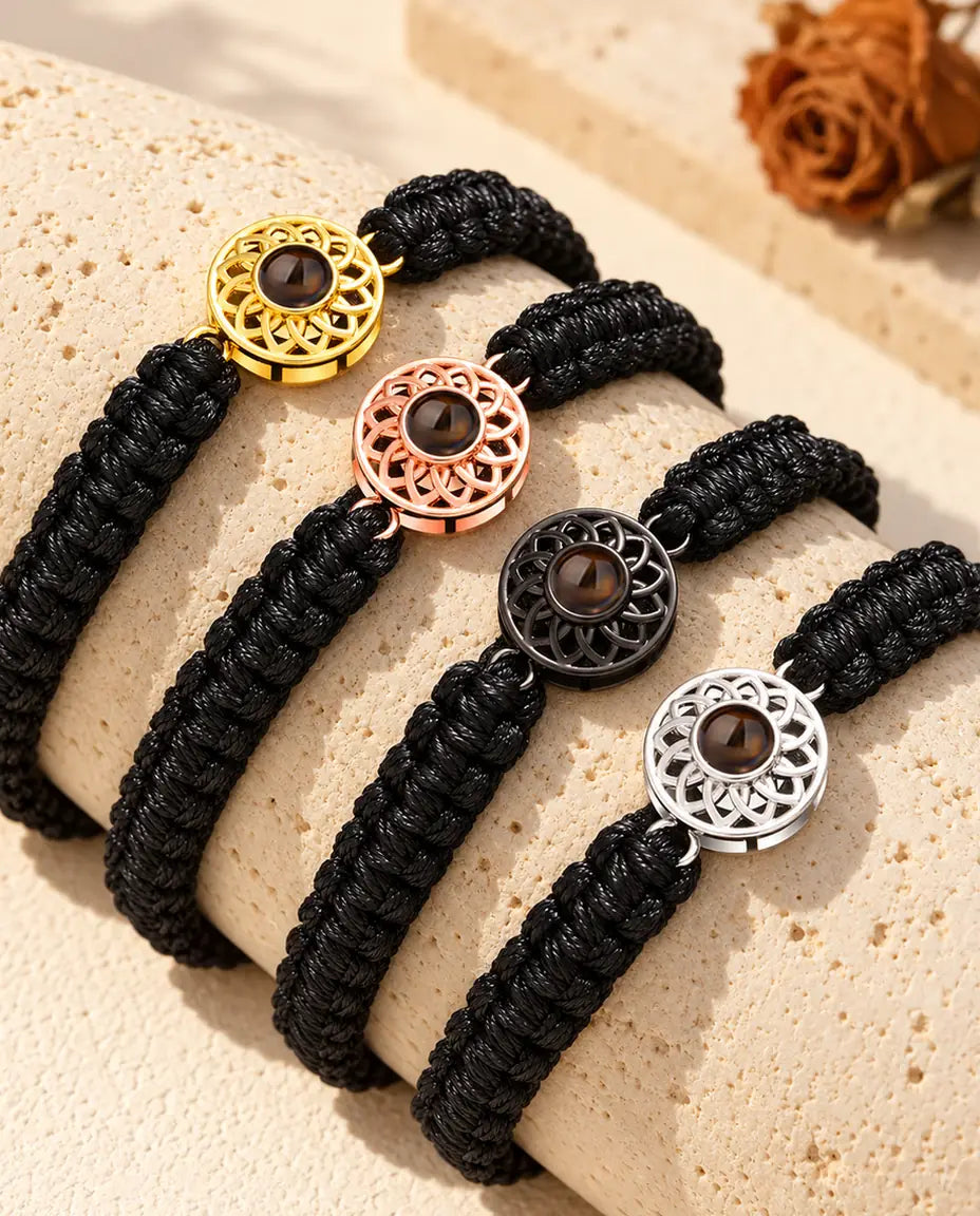 Quattro bracciali con cordino intrecciato nero in tutti i colori del charm, appoggiati sul travertino