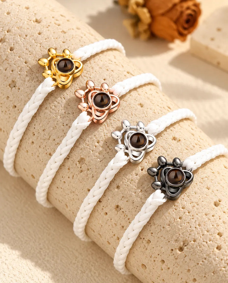 Bracciali su cordino intrecciato bianco con charm a zampa allineati, uno per ogni colore del charm