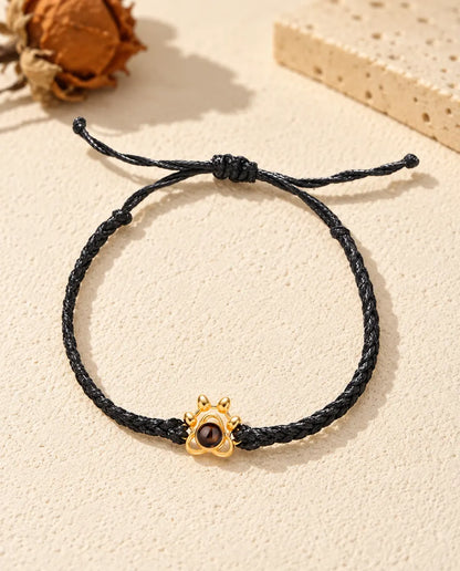 Vista dall'alto del bracciale con charm a zampa dorato su cordino intrecciato nero e nodo scorrevole