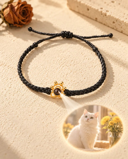 La luce attraverso la pietra marrone del charm a zampa dorato proietta sul gesso la foto rotonda di un gatto