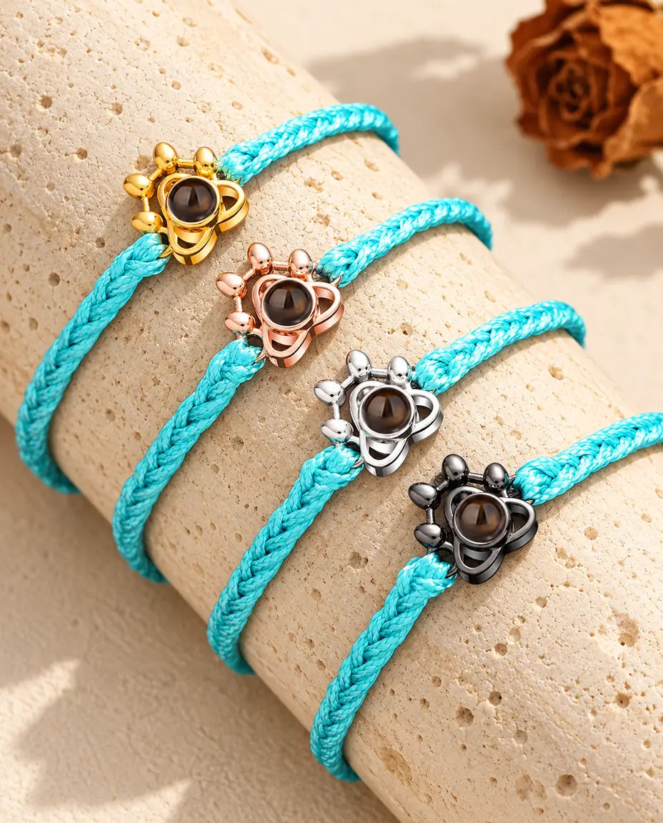 Quattro bracciali su cordino blu con charm a zampa dorato, color oro rosa, argento e nero su travertino