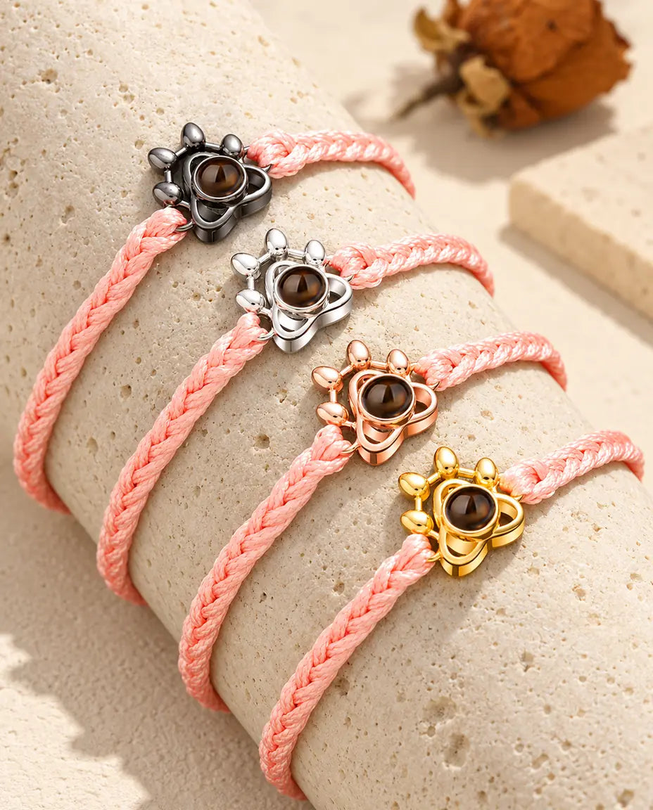 Bracciali su cordino intrecciato rosa con charm a zampa in tutti i colori, adagiati sul travertino