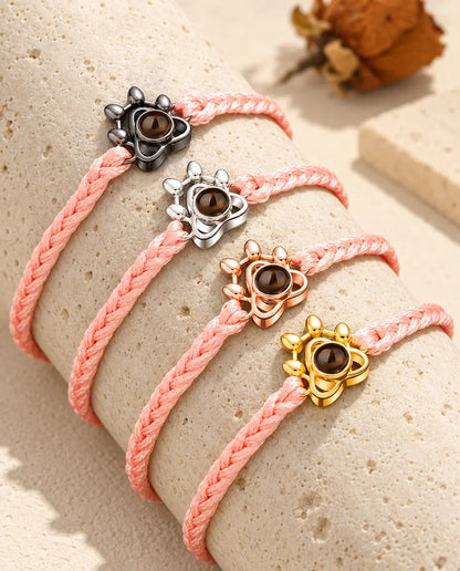 Bracciali su cordino intrecciato rosa con charm a zampa in tutti i colori, adagiati sul travertino