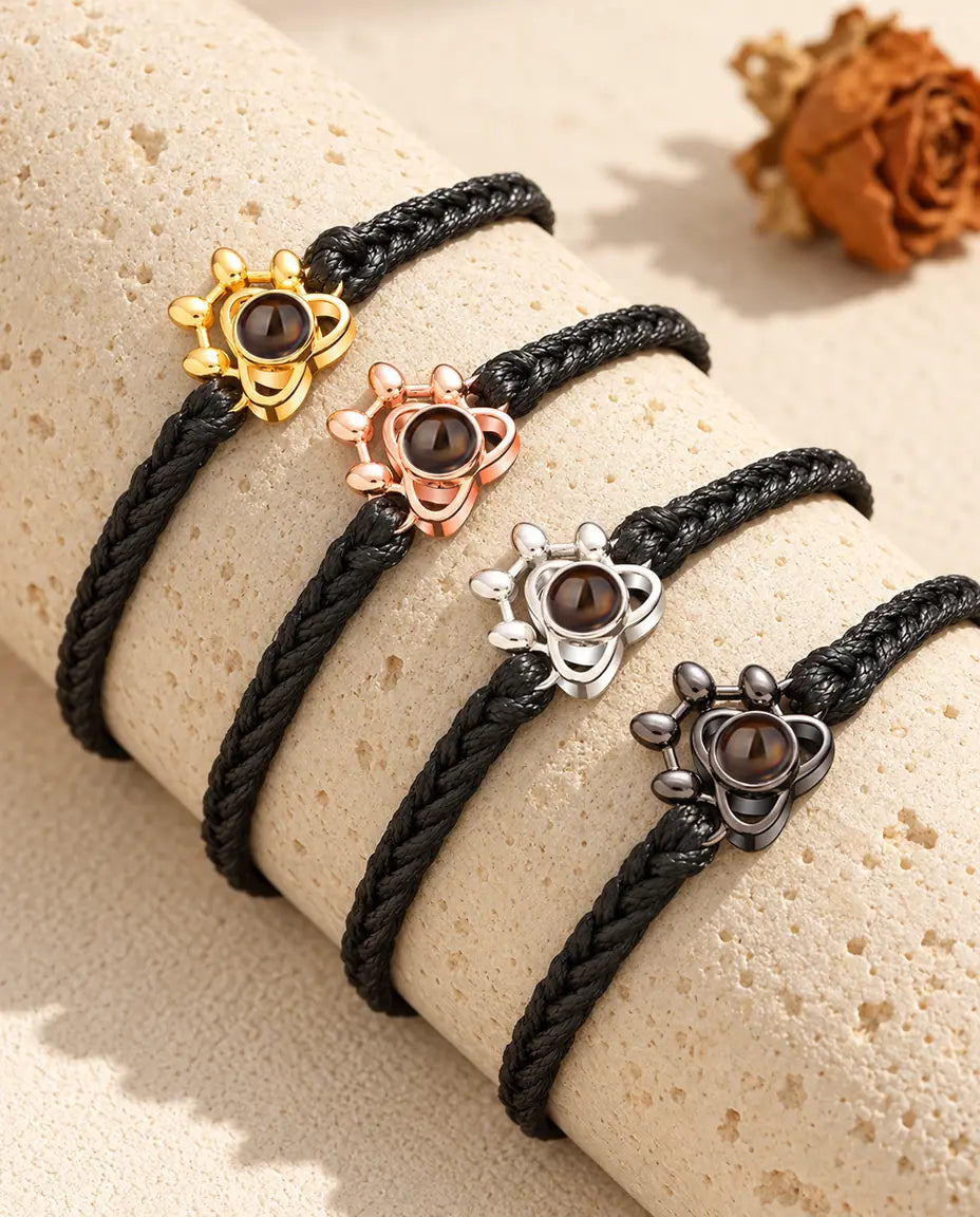 Quattro bracciali su cordino intrecciato nero con charm a zampa in ogni colore su un blocco di travertino
